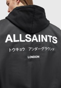 Crna kapuljača jakna sa bijelim natpisom: "ALLSAINTS," japanskim znakovima i "LONDON" na leđima. Glatka tekstura, ležerni dizajn.