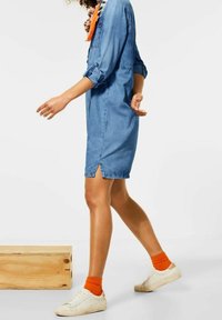 Džínová šatová košile s ohrnutými rukávy, bočními rozparky a volným střihem. V kombinaci s oranžovými ponožkami a bílými teniskami.