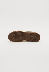 Barna gumitalp zigzag mintázattal és kör alakú tapadó pontokkal. Simább külső él és középső logó részlet. Texturált felület a tapadásért.