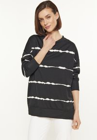 Felpa nera con motivo a strisce ondulate bianche, vestibilità oversize, maniche lunghe, scollatura tonda e polsini rigati. Tessuto morbido.
