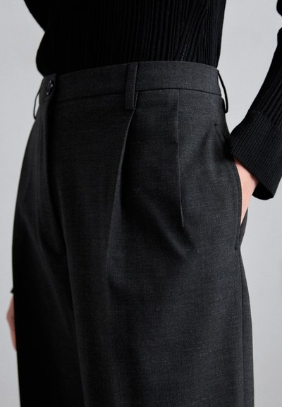 Pantaloni grigio scuro su misura con fronte piatto, tasche laterali e una cintura testurizzata, realizzati in un tessuto liscio e strutturato.