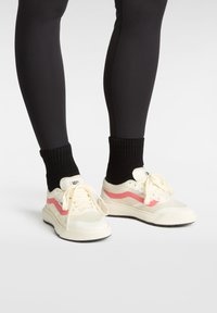 Zapatillas blancas con un detalle de ola rosa, malla texturizada y cuero suave, combinadas con calcetines negros acanalados y leggings negros ajustados.
