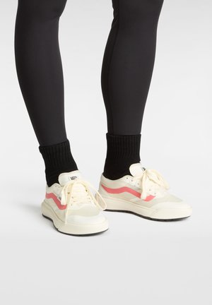 Sneaker bianche con un dettaglio a onda rosa, mesh testurizzato e pelle liscia, abbinate a calze nere a coste e leggings neri aderenti.