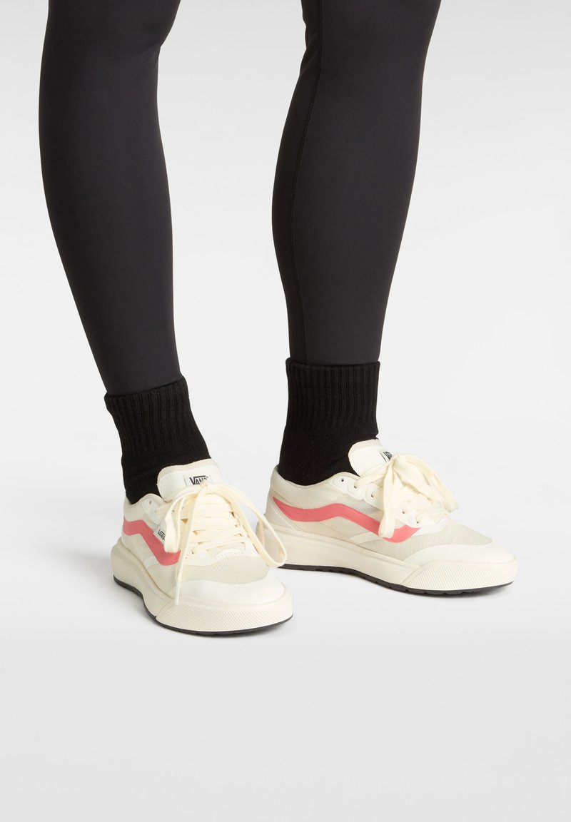 Zapatillas blancas con un detalle de ola rosa, malla texturizada y cuero suave, combinadas con calcetines negros acanalados y leggings negros ajustados.
