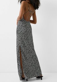 Vestido maxi floral en blanco y negro con diseño sin espalda, tirantes finos y una abertura alta en el muslo. Fabricado con tejido ligero y suave al tacto.