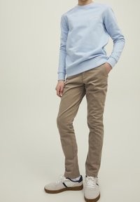 Ljusblå sweatshirt med rund halsringning och vit "SAINT TROPEZ TENNIS"-logotyp, matchad med beige byxor och vita sneakers med svarta och röda detaljer.