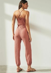 Oxblodsfärgad overall med texturerad tyg, spagettistövlar och elastisk midja. Löst sittande byxor som smalnar av vid vristerna. Sandaler kompletterar outfiten.
