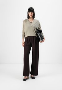 Világosszürke V-kivágású pulóver sötétbarna, bő szárú nadrággal párosítva. A modell egy fekete bőr clutch-ot tart, és fekete magassarkú cipőt visel.