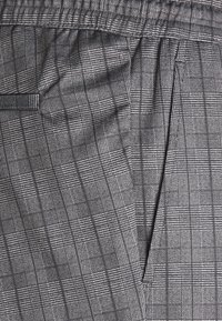 Grå rutigt tyg med ett rutigt mönster. Elastisk midja och mjuk känsla med en subtil glans. Skräddarsydd design med sidofickor.