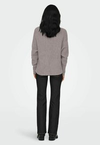 Grijze geribbelde trui met verlaagde schouders, gedragen over zwarte rechte jeans, met een relaxte pasvorm en een achteraanzicht, staande op zwarte schoenen.