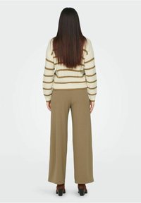 Pull en maille à rayures crème avec manches longues, associé à un pantalon large taille haute couleur olive et des bottines marron à talons blocs.