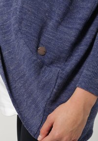 Blue knitted sweater with a textured finish, featuring a round neckline, long sleeves, and a visible logo button detail on the side.