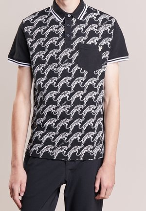 Czarna koszulka polo z krótkim rękawem z białym wzorem tygrysa i napisem "Versace Jeans", z czarną kieszenią na piersi z małym metalowym detalem w kształcie litery V.