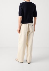 Navy knitted sweater with short sleeves and a textured pattern, paired with cream wide-leg trousers featuring back pockets and a logo tag.