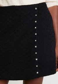 Mini-jupe noire texturée avec des accents de clous argentés sur un côté, d'une coupe légèrement ample et d'un design simple et épuré.