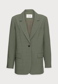 Grüne maßgeschneiderte Blazerjacke mit Reverskragen, einem schwarzen Knopf und zwei Vorderentaschen. Glatte Textur, minimalistisches Design und taillierter Schnitt.