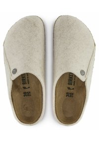 Wool felt clogs in light beige with a soft texture, rounded toe, and a subtle logo accent. Interior lining features a dark brown insole.