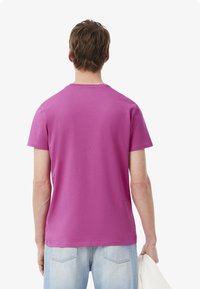 Camiseta de manga corta y cuello redondo en algodón de color rosa brillante, con una textura suave y sin patrones visibles, combinada con jeans de mezclilla claros.