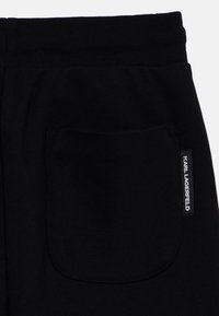 Zwarte joggings met een achterzak met een ronde vorm en een klein merklabel in het wit; gemaakt van zachte, gestructureerde stof.