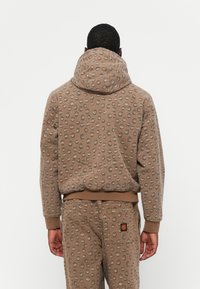 Bruine hoodie met een gestructureerd patroon van cirkelvormige stippen, met een grote capuchon, geribbelde manchetten en een relaxte pasvorm. Gecombineerd met bijpassende broek.