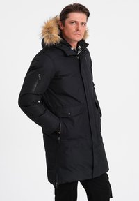 Giacca parka nera con cappuccio foderato in pelliccia, dotata di tasche con zip e a soffietto, maniche lunghe e vestibilità morbida. Tessuto liscio, materiale resistente all'acqua.