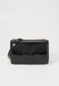 Black patent leather crossbody bag with embossed "CK" logo, silver chain accent, and adjustable strap, rectangular shape and glossy finish.