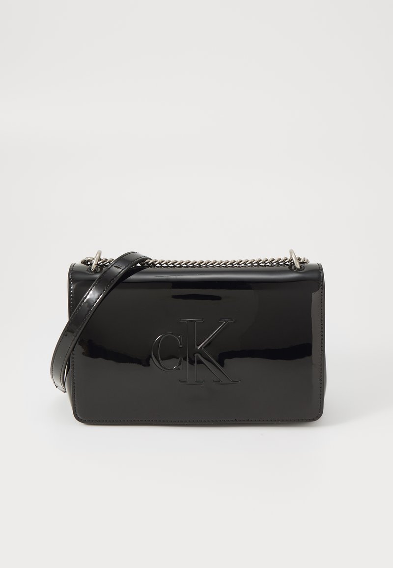 Black patent leather crossbody bag with embossed "CK" logo, silver chain accent, and adjustable strap, rectangular shape and glossy finish.