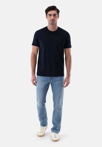 Marineblaues T-Shirt mit kurzen Ärmeln, Rundhalsausschnitt und weißem Rand, kombiniert mit hellblauen Jeans und cremefarbenen Sneakers. Glatter, lässiger Stoff.