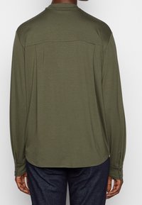 Olijfgroene shirt met lange mouwen, een relaxte pasvorm, rugdetail en knoopmanchetten, gemaakt van zachte, lichte stof.