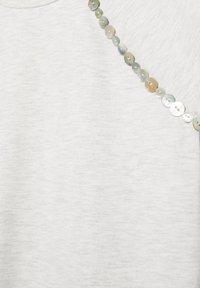 Tissu gris clair avec une rangée diagonale de petits boutons ronds brillants en nacre à deux trous.