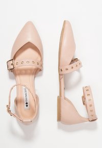 Bailarinas de imitación de cuero en color rosa, con punta afilada, tira en el tobillo y acentos de tachuelas doradas. Textura suave y tacón bajo para mayor comodidad.