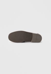 Suela de zapato de vestir de cuero marrón oscuro para hombre con textura antideslizante y la marca "CALL IT SPRING" sobre un fondo blanco liso.