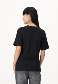 T-shirt in cotone nero con maniche corte, scollatura rotonda e vestibilità rilassata, abbinato a jeans grigi sbiaditi. Il tessuto appare liscio e leggero.