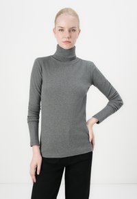 Grijze coltrui gemaakt van zachte, gestructureerde stof met lange mouwen, een getailleerde pasvorm en een gladde afwerking. Gecombineerd met zwarte broek.