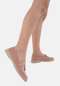 Jasnoróżowe zamszowe loafersy z płaską beżową podeszwą, z akcentem w postaci kokardy i widocznym przeszyciem wzdłuż krawędzi.