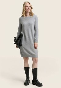 Szürke kötött ruha hosszú ujjakkal, kerek nyakkivágással és bordázott szegéllyel. Térd fölé érő fekete csizmával és fekete kézitáskával párosítva. Sima textúrájú.