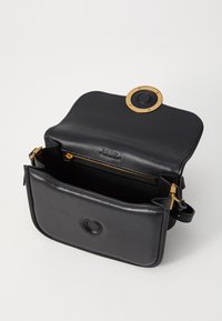 Black leather handbag with a rounded gold hardware detail and an exterior pocket. Features a zippered compartment and adjustable strap.