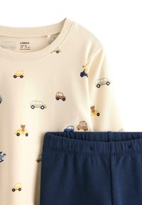 Top beige chiaro con stampe di auto e animali colorati, abbinato a pantaloni con elastico in vita blu scuro. Realizzato in tessuto morbido.