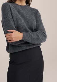 Grå stickad tröja med rund hals och långa ärmar, med en mjuk textur och avslappnad passform, i kombination med en svart pennkjol.