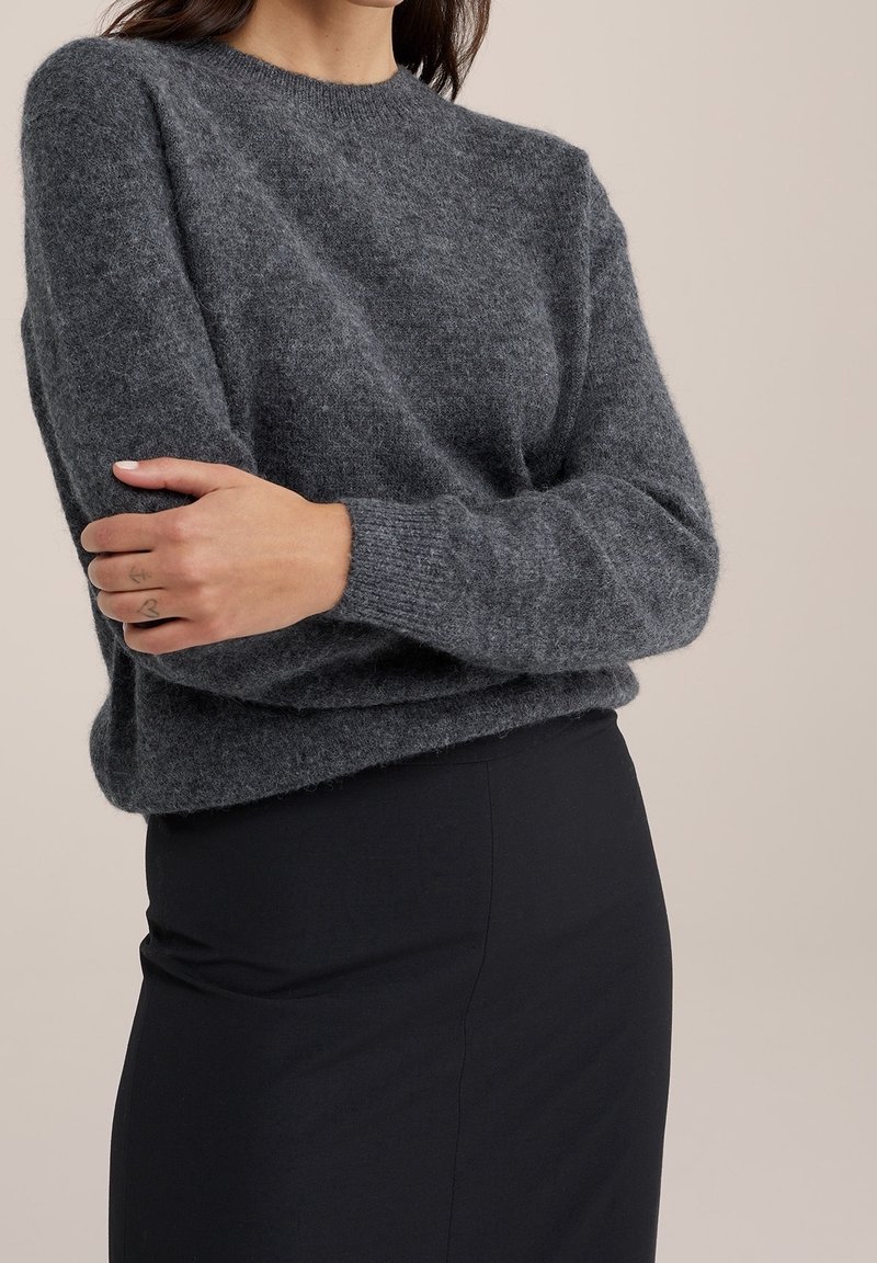Grå stickad tröja med rund hals och långa ärmar, med en mjuk textur och avslappnad passform, i kombination med en svart pennkjol.