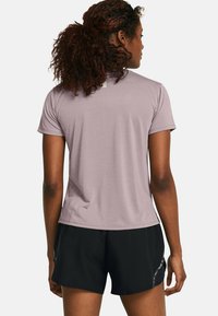 Camisa atlética de manga corta, de color púrpura claro y con una textura suave, combinada con pantalones cortos negros que cuentan con un sutil detalle reflectante en el costado.