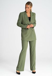 Oliwkowa marynarka szyta na miarę oraz dopasowane spodnie z gładkiego materiału. Marynarka ma pojedyncze zapięcie na guzik i klapy w kształcie litery V.