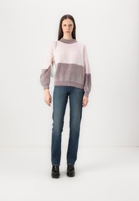 Maglione lavorato a maglia rosa chiaro con maniche a palloncino, striscia rosa scuro, abbinato a jeans di denim blu e scarpe nere. Accessorio borsa bianca semplice.