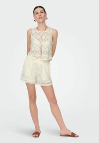 Kanten gebreide mouwloze top en shorts set in crème. Kenmerkt zich door diamantpatronen, een elastische tailleband en casual schuifsandalen in bruin.