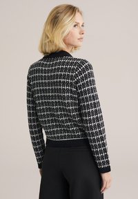 Čierno-biely sveter s vzorom, s rebrovaným golierom a manžetami. Má skrátený strih a textúrované pletenie, ktoré zdôrazňuje kockovaný motív.