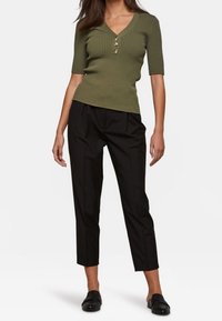 Top de canalé color verde oliva con mangas cortas y tres botones frontales, combinado con pantalones cortos negros de tiro alto y zapatos negros de tipo mocasín.