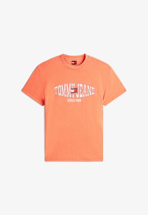 Πορτοκαλί T-shirt με κοντά μανίκια και στρογγυλή λαιμόκοψη, με το λογότυπο "TOMMY JEANS" σε λευκό και ναυτικό μπλε στο κέντρο, και την επιγραφή "SINCE 1985" τυπωμένη από κάτω.