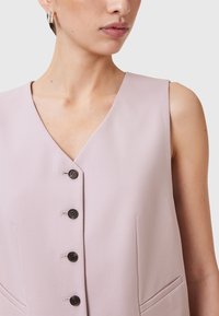 Gilet senza maniche di un delicato rosa, con scollo a V, cinque bottoni neri sul davanti e tasche laterali per un tocco in più. Texture liscia e morbida.