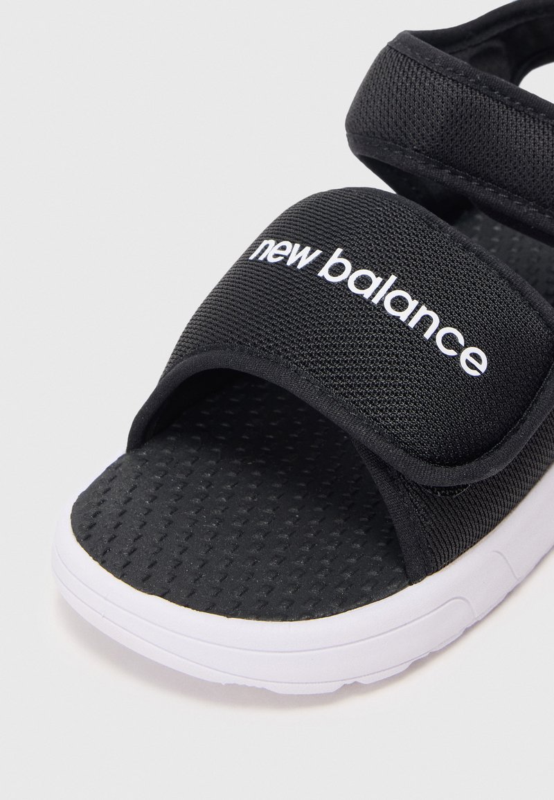 Zwarte New Balance-sandaal met een textiel bovenwerk, verstelbare band en wit logo; contrasterende witte zool met een gestempelde voetbed.