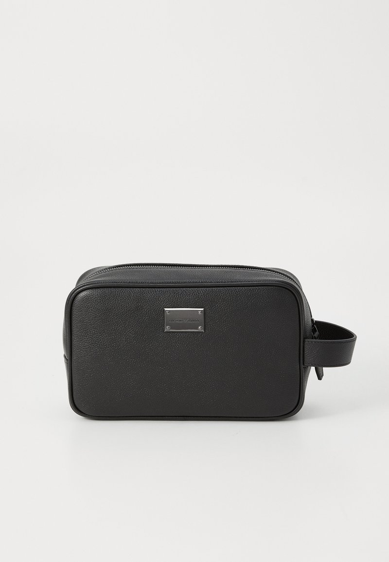 Melnas taisnstūra formas ādas tualetes somiņa ar augšējo rāvējslēdzēju, sānu rokturi un mazu metāla logo plāksnīti uz priekšējā paneļa.